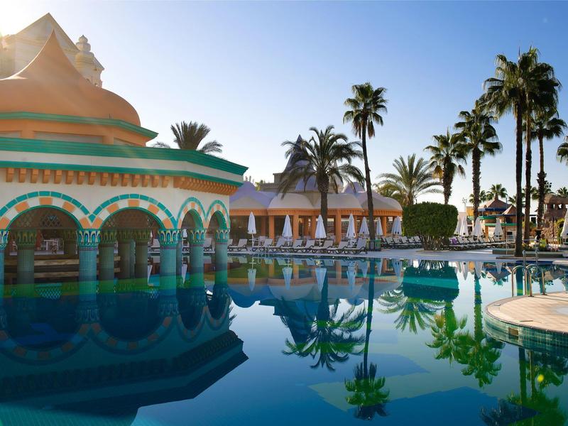 Piscina de hotel de lujo con pabellón rodeado de palmeras y agua azul clara al atardecer.