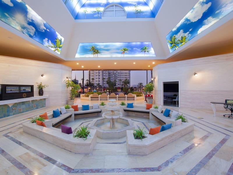 Patio interior con fuente, cojines, plantas y vista a edificios urbanos a la luz del día.