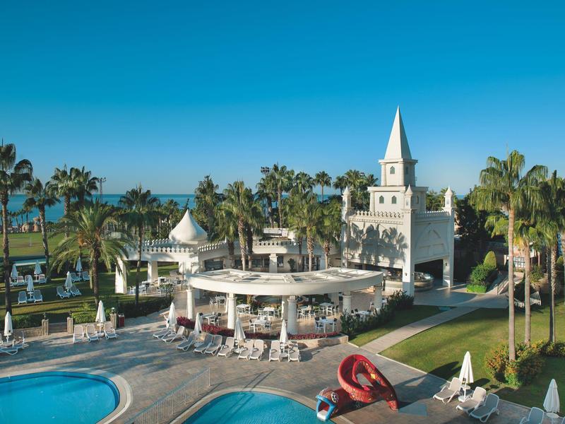 Complejo hotelero con piscina, palmeras y torre en un entorno tropical soleado junto al mar.