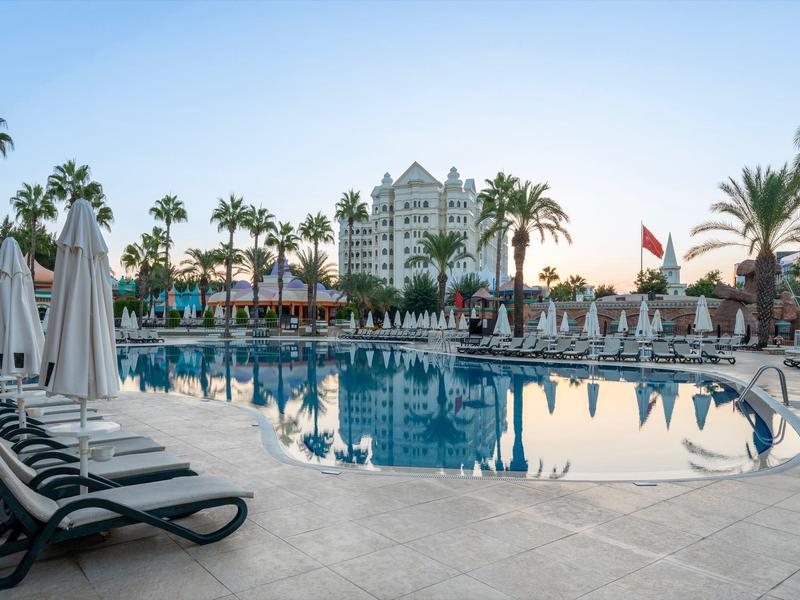 Gran piscina de hotel rodeada de palmeras y tumbonas bajo un cielo despejado.