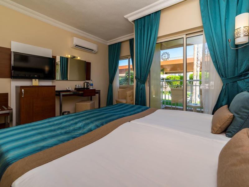 Habitación de hotel moderna con cama grande, TV, escritorio y balcón con vistas.