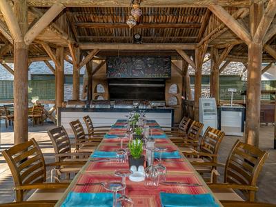 Rustykalna zadaszona przestrzeń na zewnątrz z długim stołem jadalnym, kolorowymi obrusami i drewnianymi meblami.