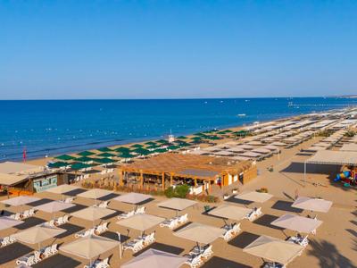 Długa piaszczysta plaża z rzędami parasoli i leżaków nad morzem pod niebieskim niebem.