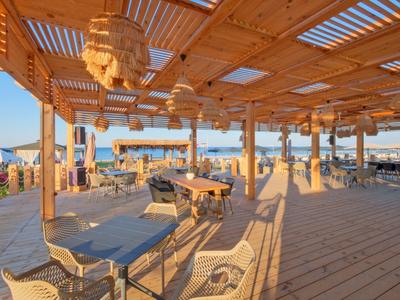 Otwarty drewniany pawilon z miejscem do siedzenia i widokiem na morze o zachodzie słońca.