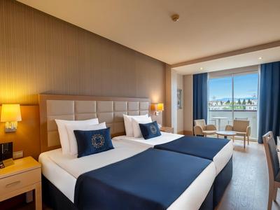 Camera d'hotel con due letti singoli, biancheria blu e bianca e balcone con vista.