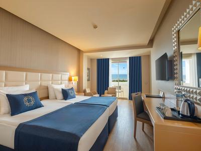 Nowoczesny pokój hotelowy z dwoma łóżkami, biurkiem, telewizorem i balkonem z widokiem na morze.