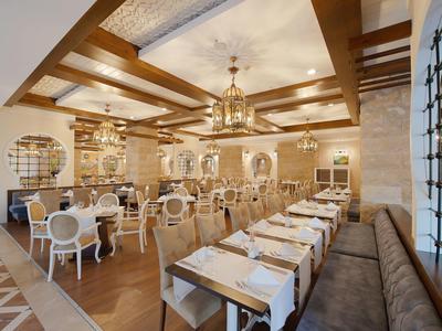 Elegancko urządzona jadalnia z drewnianym stropem, żyrandolami i rzędami stołów z białymi krzesłami.