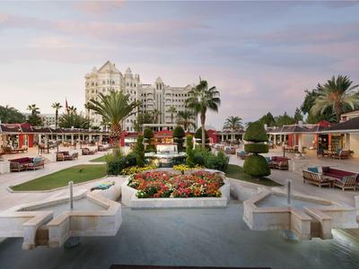 Duży ogród hotelowy z miejscami do siedzenia, kwietnikami i palmami o zachodzie słońca.