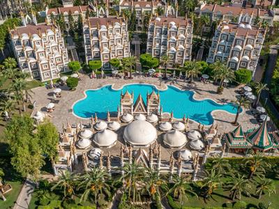 Widok z lotu ptaka na hotel z dużym, unikalnie ukształtowanym basenem, otoczony ogrodami i budynkami.