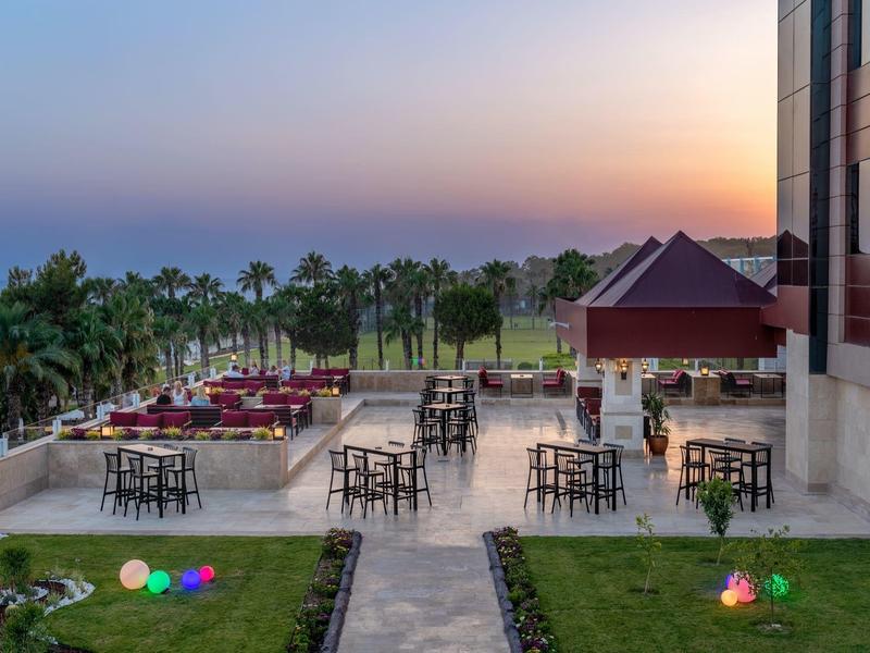 Taras z stolikami i krzesłami przed hotelem z widokiem na palmy i zachód słońca nad morzem