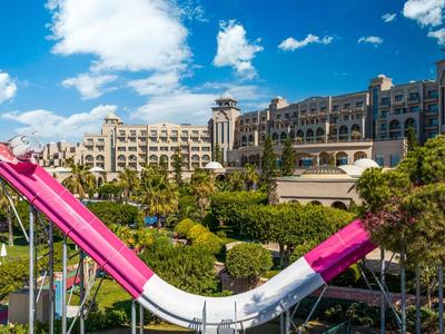 Large colorful water slide area in front of a luxury hotel under a blue sky.
