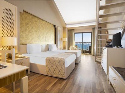 Nowoczesny pokój hotelowy z podwójnym łóżkiem, biurkiem, telewizorem i balkonem z widokiem na morze.