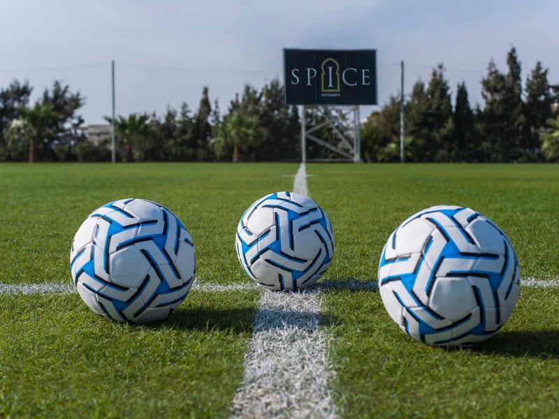 Trzy białe piłki do piłki nożnej z niebieskim wzorem na zielonej trawie przed znakiem.