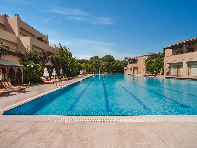 Duży basen na zewnątrz z leżakami i budynkami w tle pod niebieskim niebem.