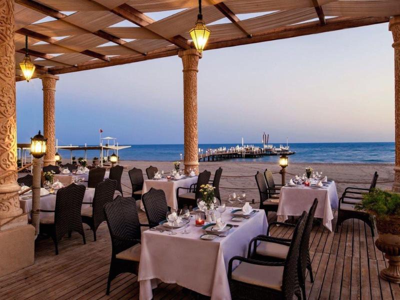 Taras restauracyjny nad morzem z nakrytymi stołami i widokiem na port o zachodzie słońca.