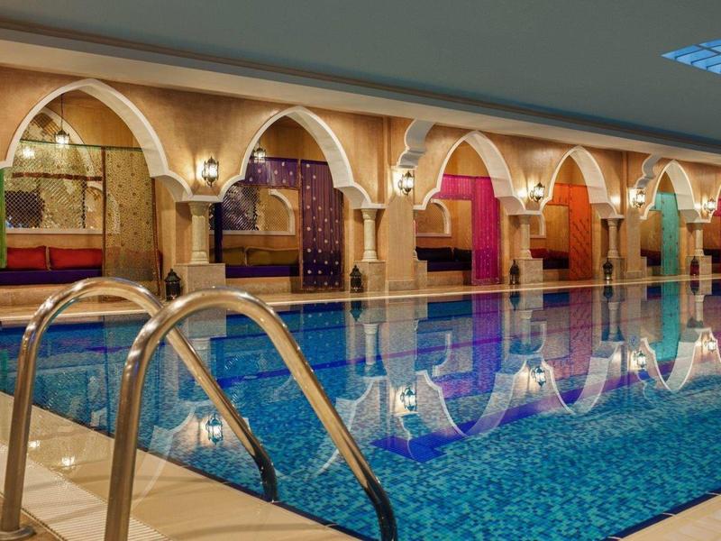 Basen wewnętrzny z niebieską wodą, mozaikowymi kafelkami i arabskimi łukami