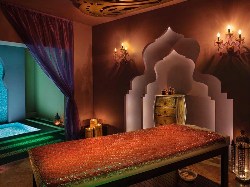 Przytulny pokój z orientalnym wystrojem i stołem do masażu, ciepłe oświetlenie.