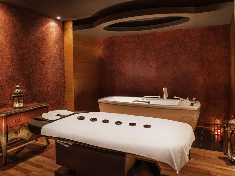 Przytulny pokój wellness z łóżkiem do masażu i wanną w ciepłych ziemistych kolorach.