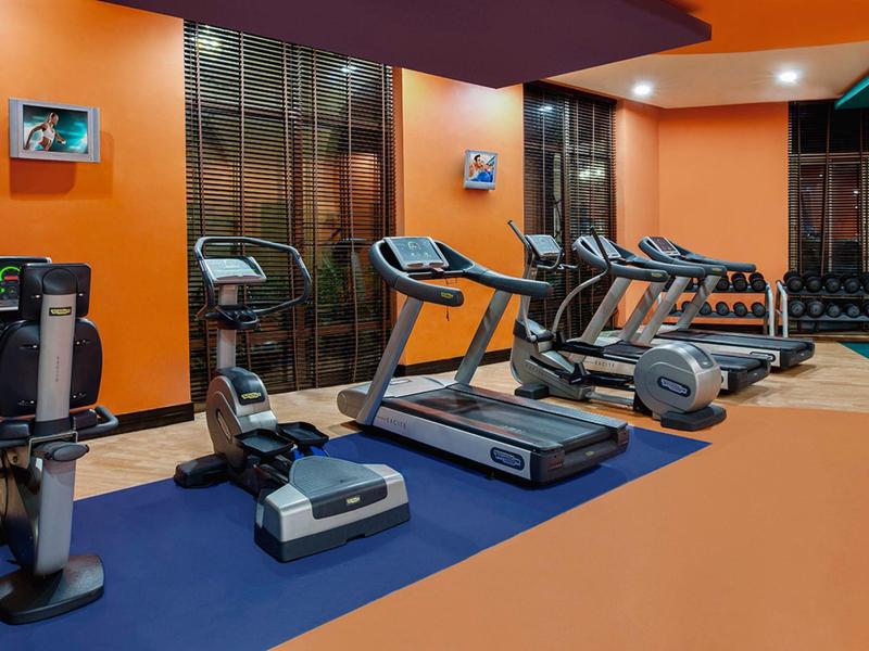 Nowoczesna siłownia z bieżniami i sprzętem do ćwiczeń w ciepłym, pomarańczowym pomieszczeniu.
