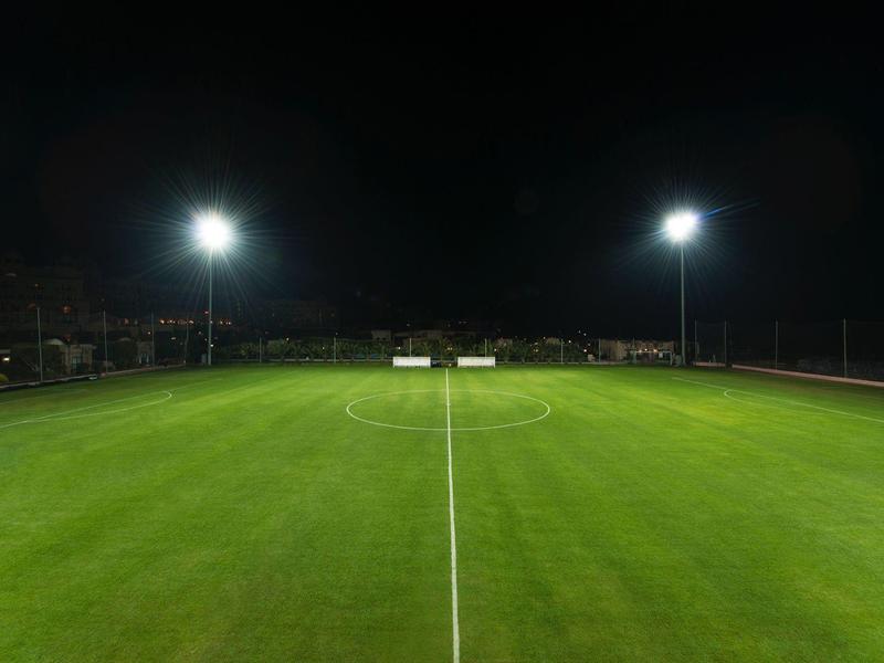 Oświetlone boisko sportowe nocą z zieloną trawą i białymi oznaczeniami