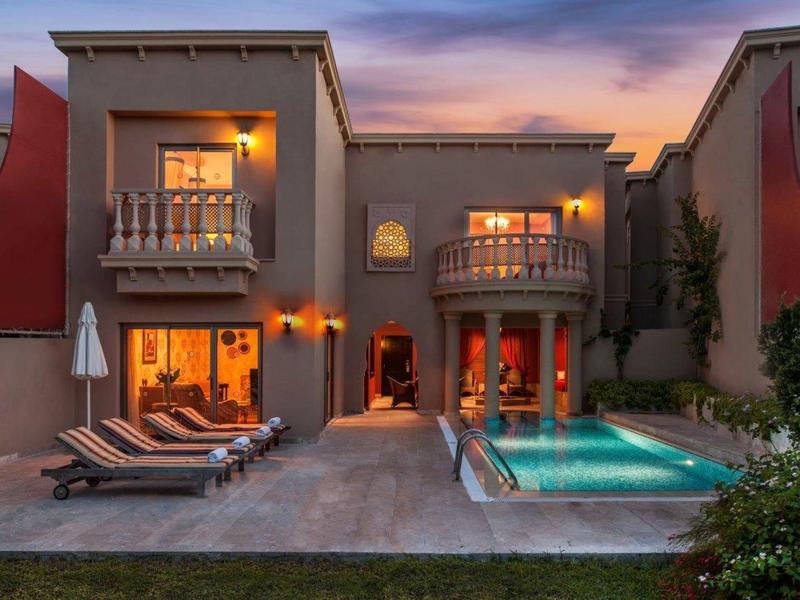Nowoczesna willa z basenem i leżakami o zachodzie słońca.