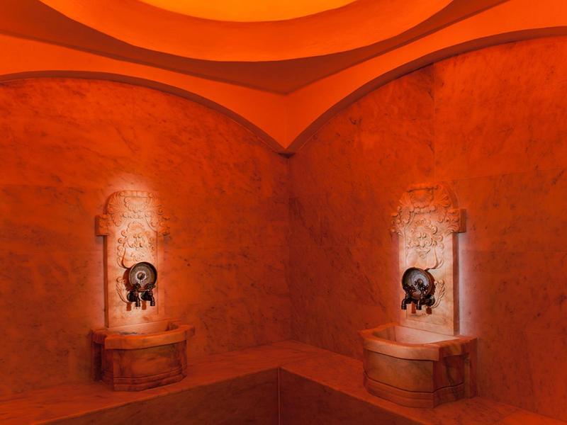 Ciepły pokój spa z pomarańczowo oświetlonymi ścianami i dwoma dekoracyjnymi fontannami.