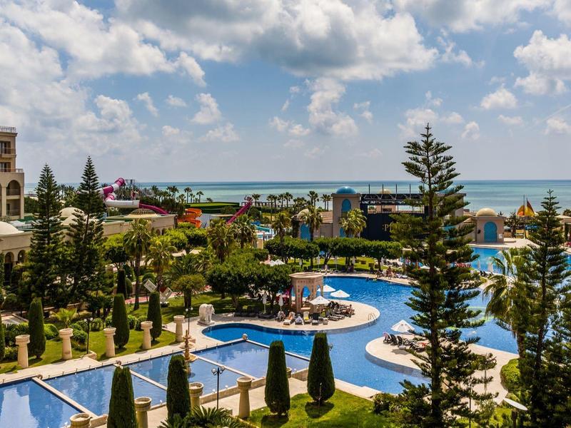 Luksusowy kompleks hotelowy z kilkoma basenami, palmami i bezpośrednim widokiem na morze pod pochmurnym niebem.