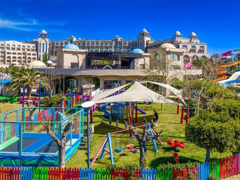 Kolorowy plac zabaw przed dużym hotelem z zjeżdżalniami wodnymi pod niebieskim niebem.