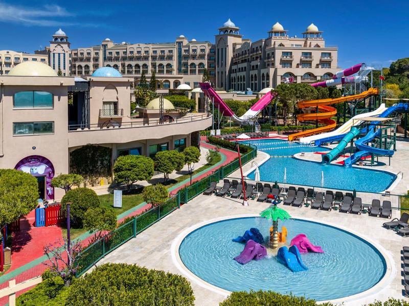 Duży kompleks hotelowy z zjeżdżalniami wodnymi i kilkoma basenami w słonecznym otoczeniu.