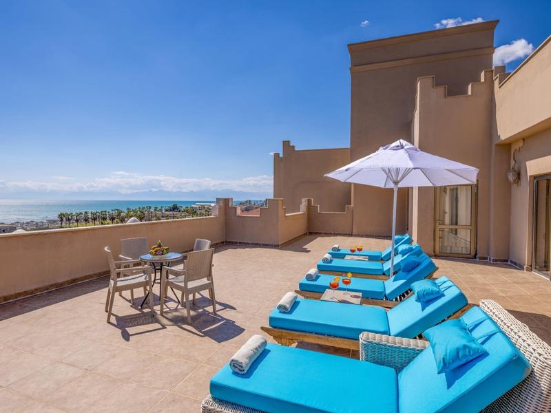 Taras z niebieskimi leżakami, parasolem i widokiem na morze przy czystym niebie.