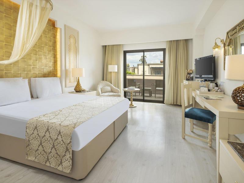 Nowoczesny pokój hotelowy z dużym łóżkiem, balkonem i jasnymi drewnianymi meblami.