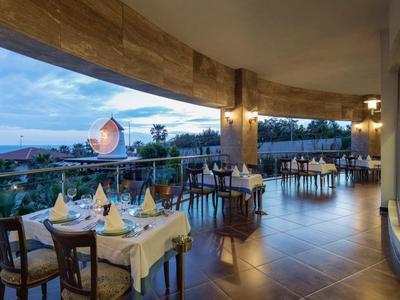 Offenes Restaurant mit gedeckten Tischen, Meerblick und bewölktem Himmel bei Sonnenuntergang.