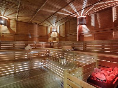 Innenraum einer Sauna mit Holzbänken, Holzwänden und roten heißen Steinen im Ofen.