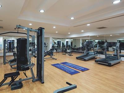 Großer, heller Fitnessraum mit Holzfußboden, Geräten, Laufbändern und großen Spiegelwänden.