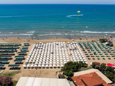 Strand mit Reihen von Sonnenschirmen und Liegestühlen sowie blauem Meer und Menschen am Ufer.