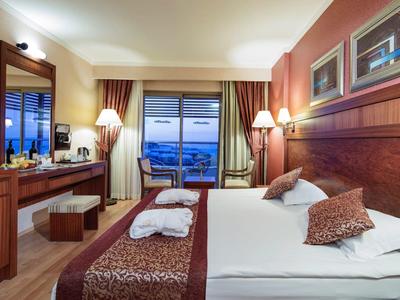 Gemütliches Hotelzimmer mit Bett, Fernseher, Schreibtisch und Balkon mit Meeresblick.