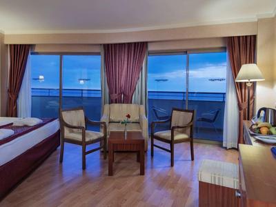 Hotelzimmer mit zwei Betten, Stühlen, großem Fenster mit Vorhängen und Blick auf Wasser bei Abenddämmerung.