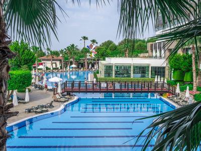 Una piscina azzurra limpida in un resort alberghiero, circondata da palme e lettini.