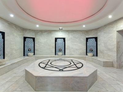 Hammam turco moderno circolare con marmo e motivi geometrici sotto illuminazione rossa sul soffitto.