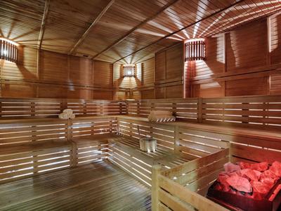 Sauna in legno con panchine a più livelli e pietre calde rosse nell'angolo.