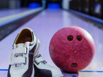 Schwarze und weiße Bowlingschuhe neben einer roten Bowlingkugel auf einer Bowlingbahn.