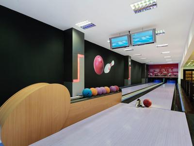 Moderne Bowlingbahn mit bunten Kugeln, zwei Bildschirmen und schwarzer Wand.
