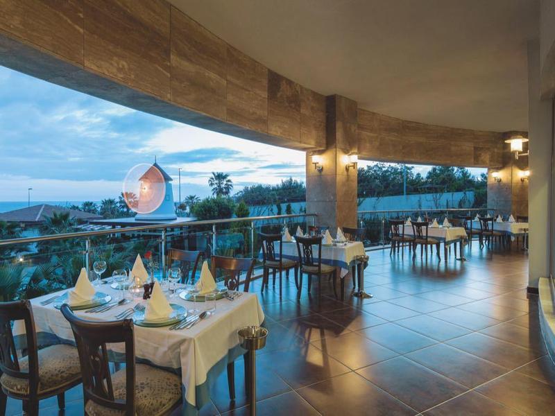 Open restaurantgedeelte van het hotel met gedekte tafels en uitzicht op zwembad en zee bij zonsondergang.