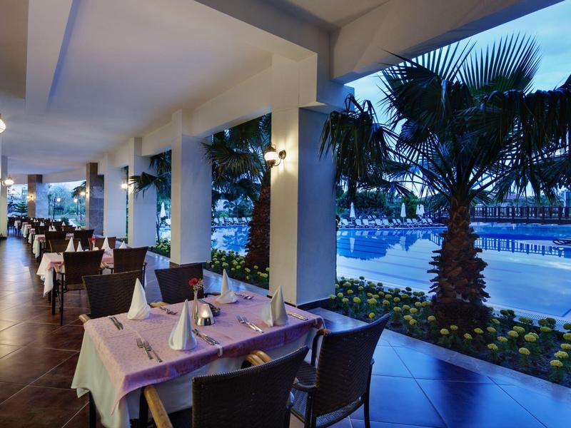 Buitencentrum restaurant bij hotel met stijlvolle tafels en uitzicht op zwembad en palmbomen bij schemering.