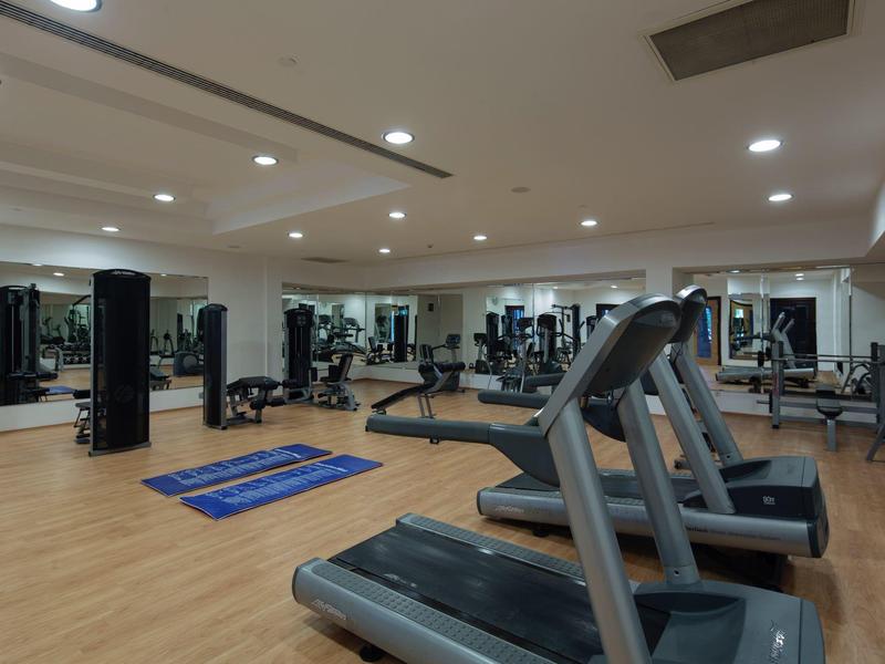 Moderne sportschool met loopbanden, fitnessapparaten en blauwe matten op een houten vloer.