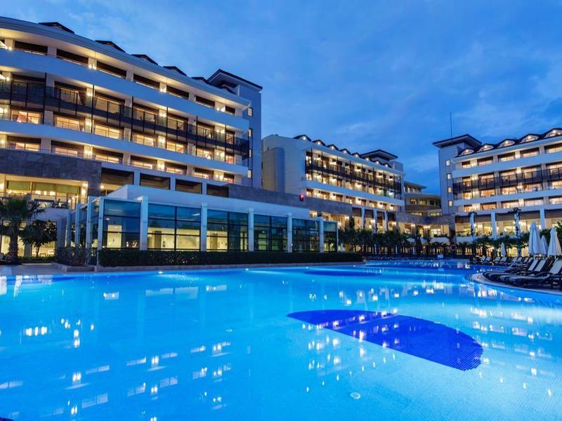 Modern hotelcomplex met verlicht zwembad bij schemering en blauwe lucht.