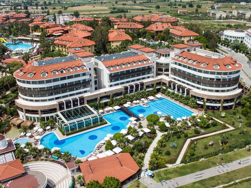 Groot hotel met meerdere zwembaden en rode daken in een groene omgeving.