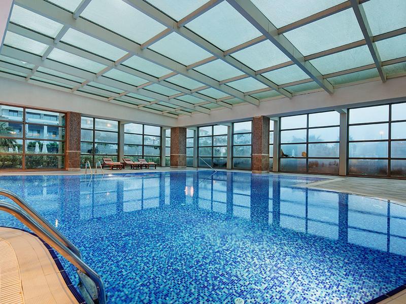 Overdekt zwembad met blauwe tegels en grote ramen met uitzicht op bergen.