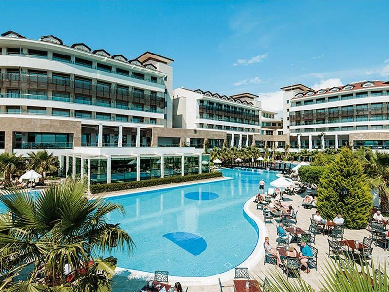 Groot hotel met twee ronde gebouwen en groot zwembad in een zonnige omgeving met palmbomen.