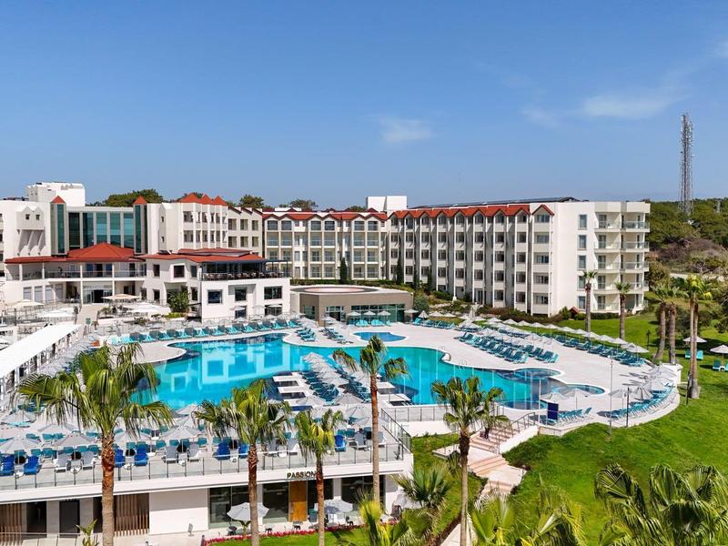 Large hotel resort with pool, umbrellas, and lounge chairs in a tropical setting.